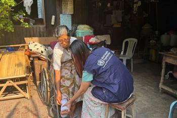 A WHO staff member examines an older woman who suffered a leg injury.